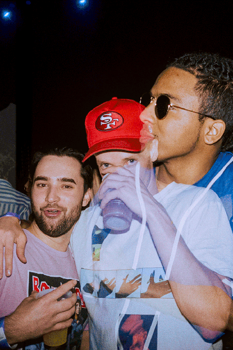 Three men are visible in a double exposure, with one man wearing a red cap and another wearing sunglasses.