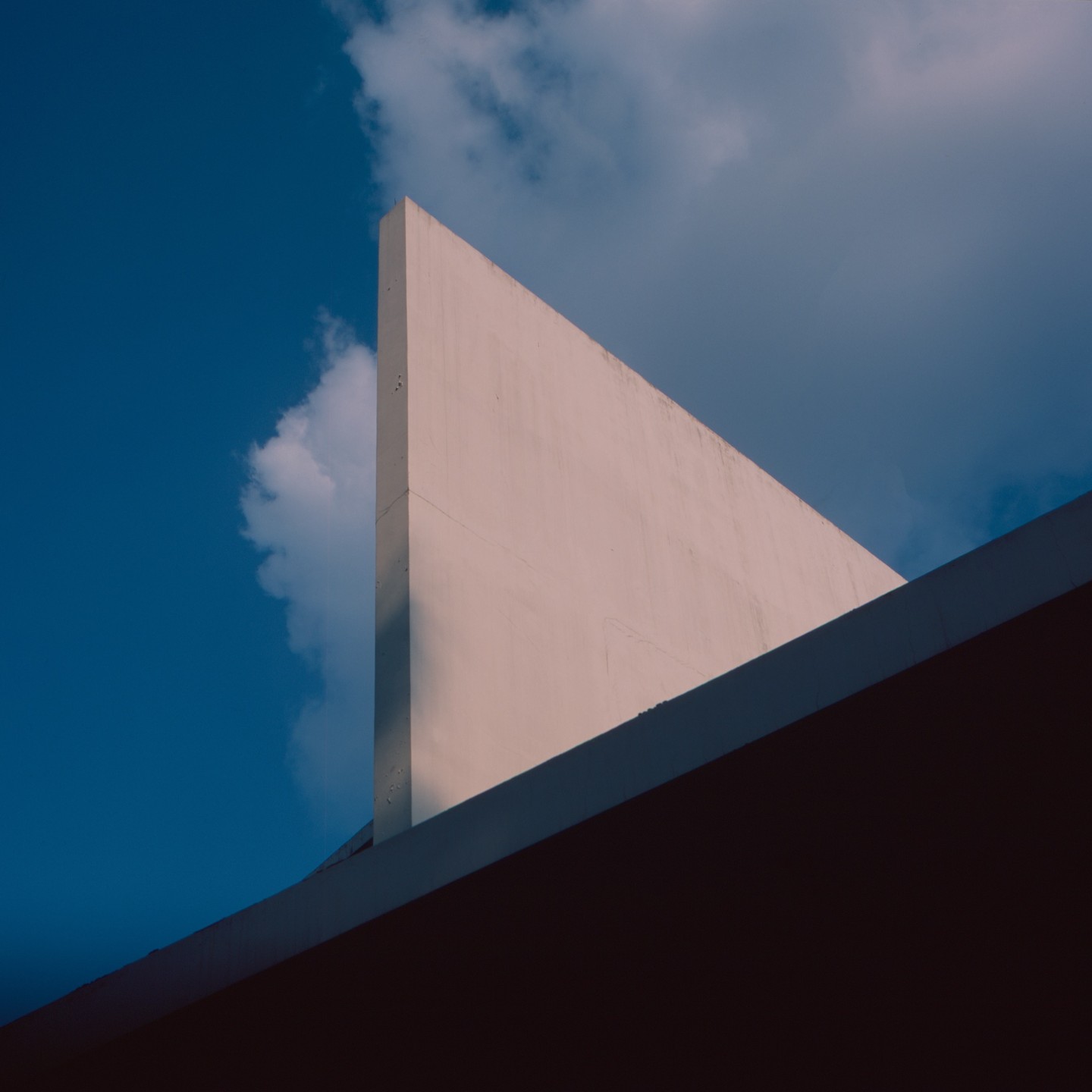 A triangular building wall is visible against a blue sky with clouds.