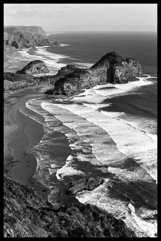 An aerial view shows a long beach with waves breaking on the shore and cliffs along the coast.