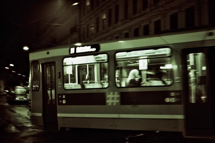A tram moves through a city street at night, with a person visible through a window.