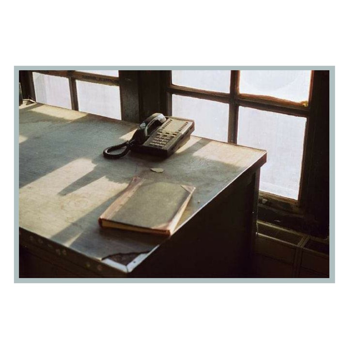 A telephone and a book sit on a desk next to a window with light streaming through.