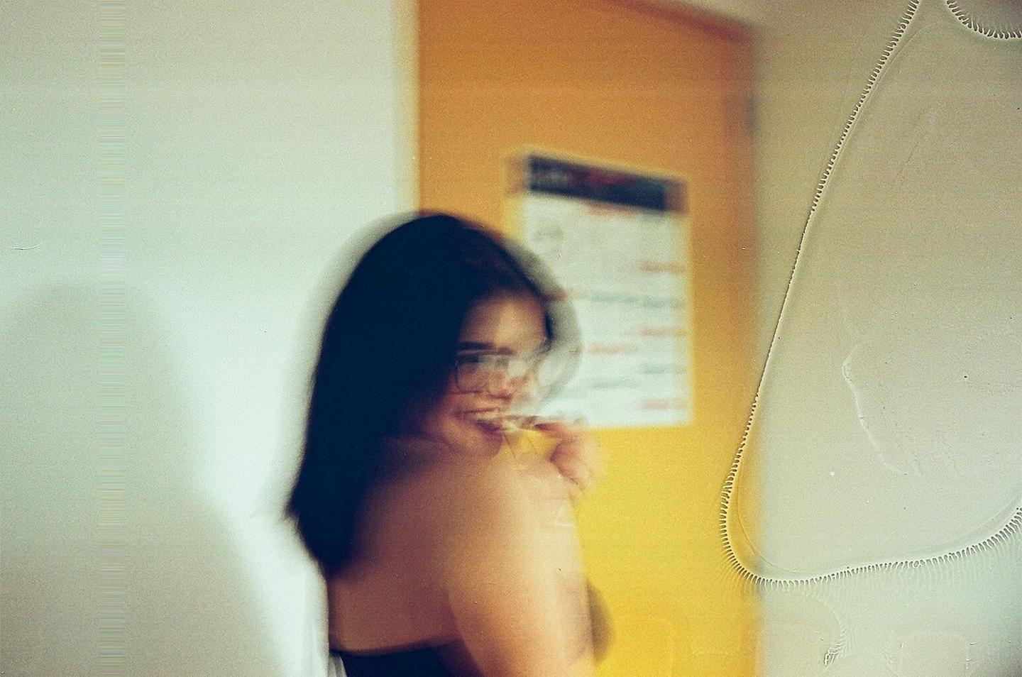 A blurry woman with glasses smiles while looking over her shoulder.