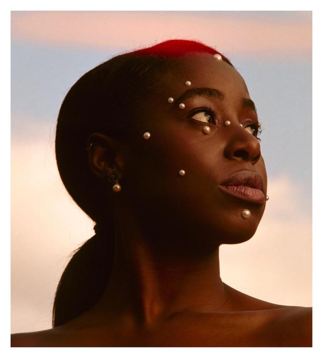A woman with pearls on her face and red hair looks up at the sky.