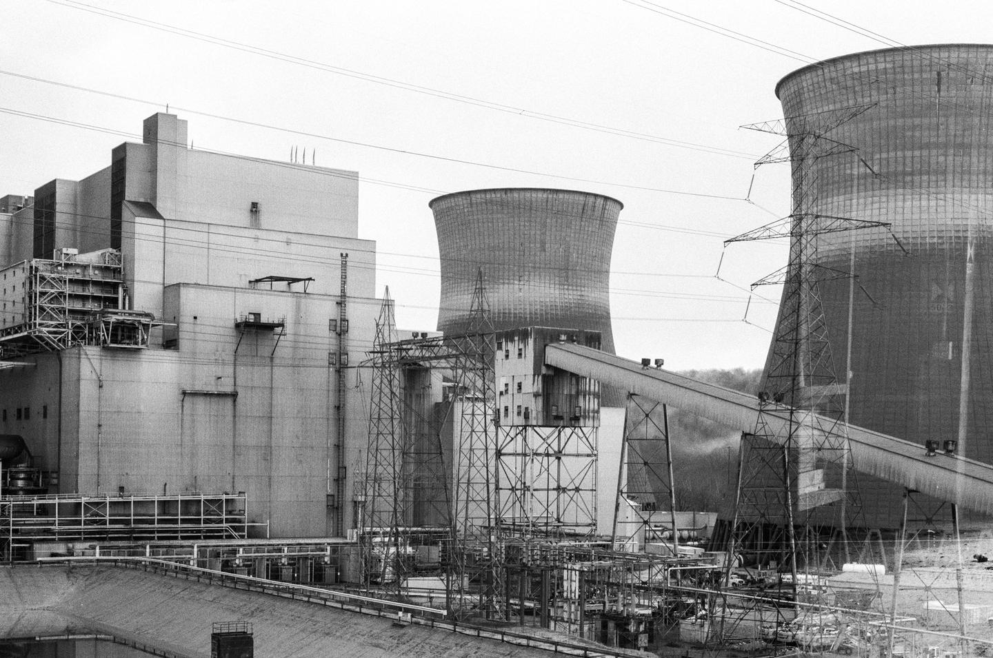 A large industrial complex with multiple cooling towers and power lines is shown under a bright sky.