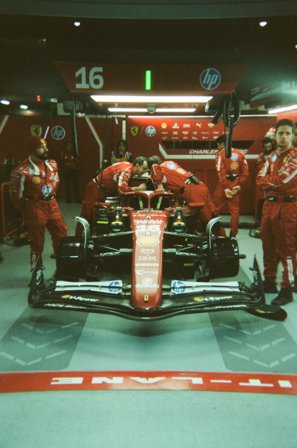 A red Formula 1 race car is surrounded by men in red racing suits in a garage.