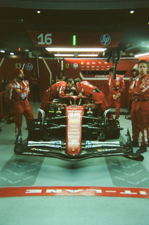 A red Formula 1 race car is surrounded by men in red racing suits in a garage.