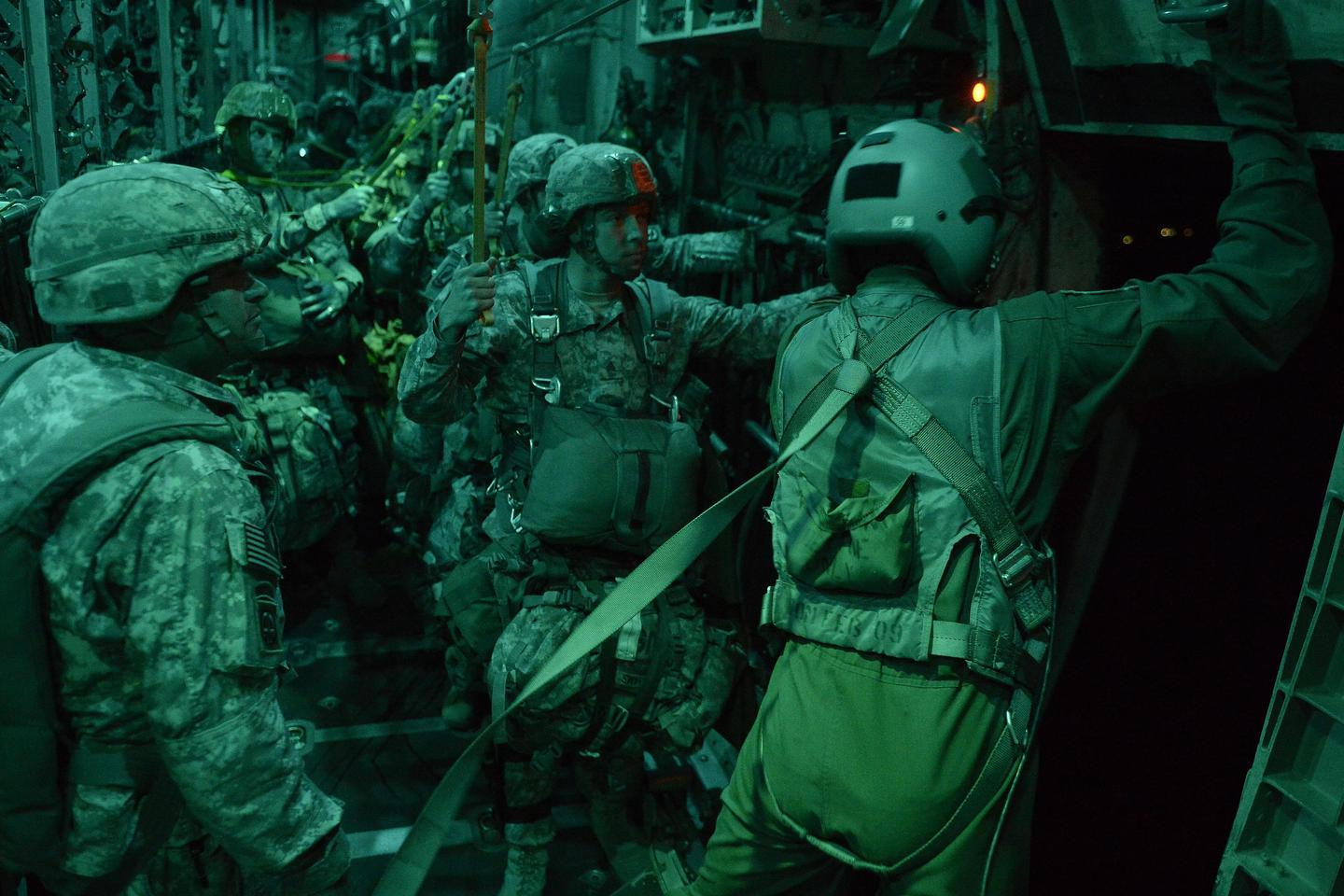 Several soldiers in camouflage and helmets are standing inside a dark aircraft.