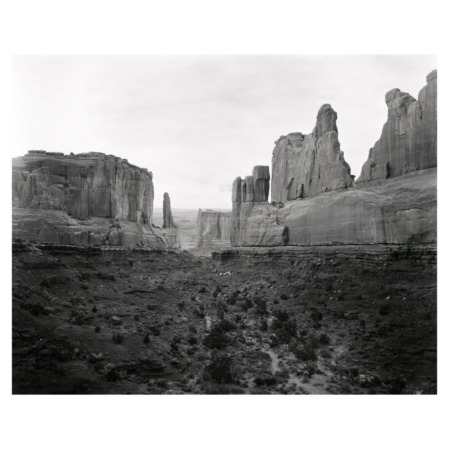 A black and white landscape shows a valley between tall rock formations under a bright sky.