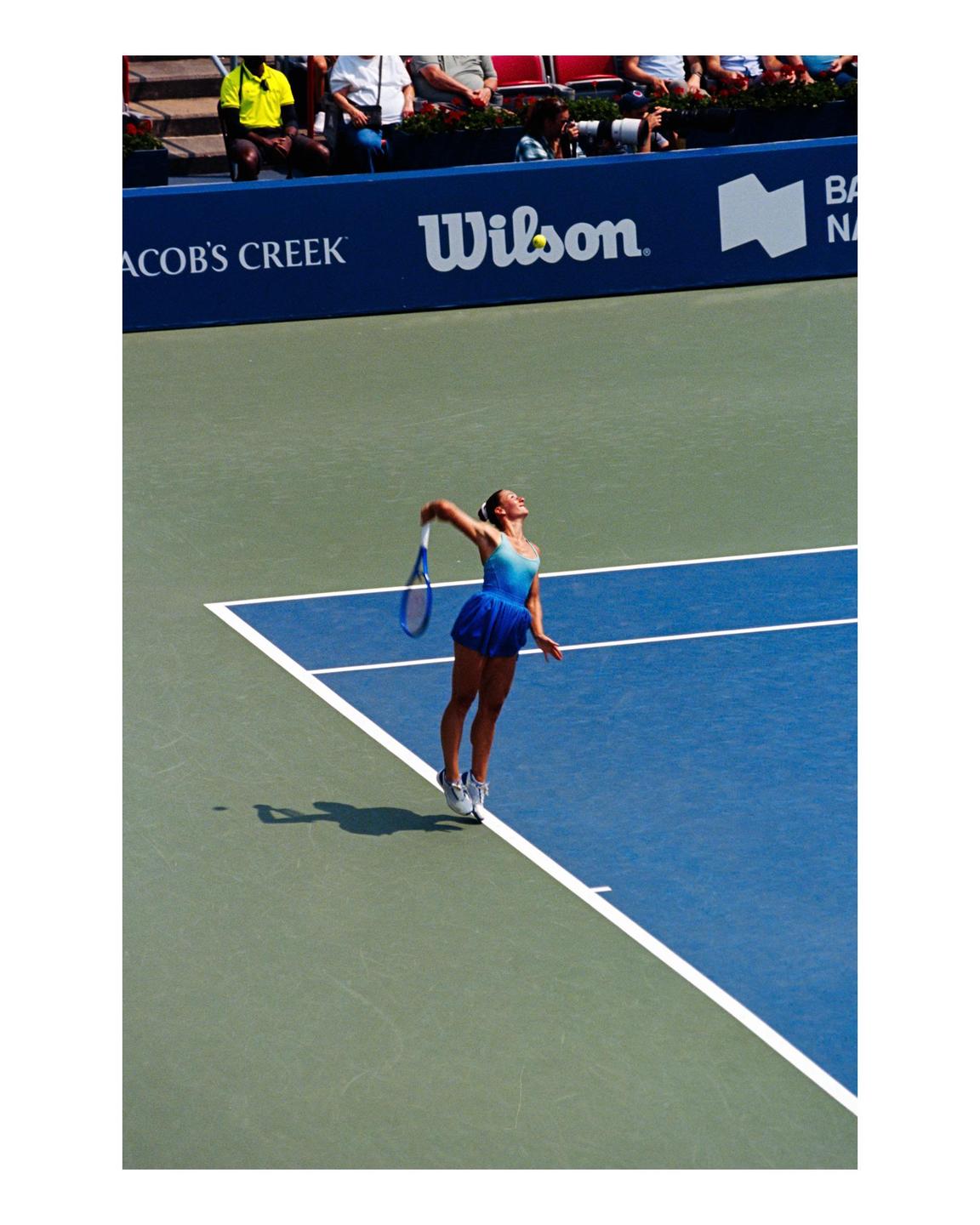 A woman in a blue dress is playing tennis on a blue and green court.