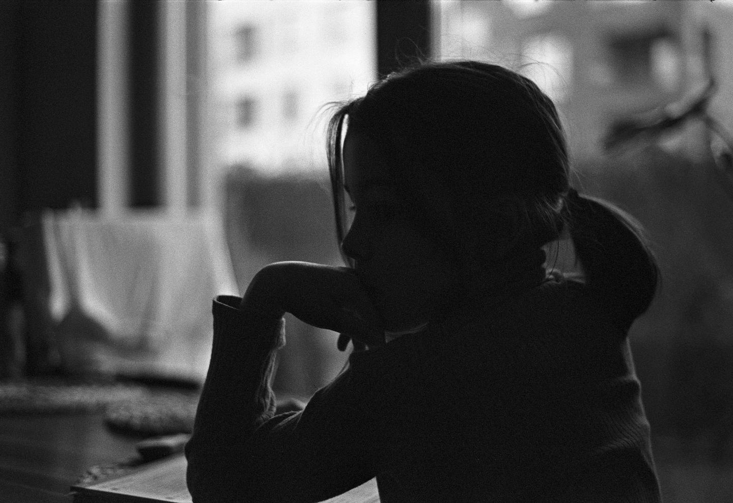 A child sits in profile with their arm resting on a table, silhouetted against a window.