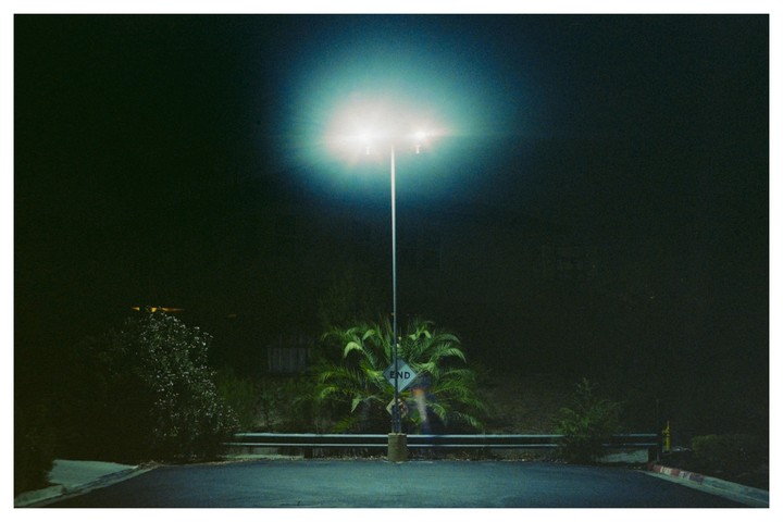 A bright street light illuminates a dark street with an "END" sign and palm trees.