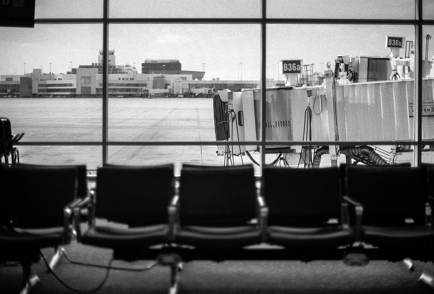 A row of empty chairs faces a large window overlooking an airport terminal and jet bridge.