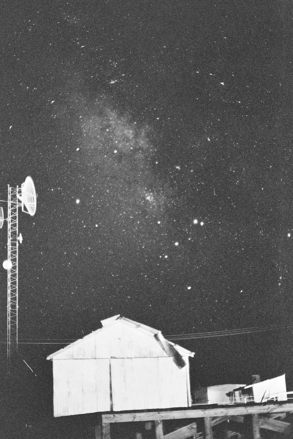 A communication tower and a small building stand under a night sky filled with stars.