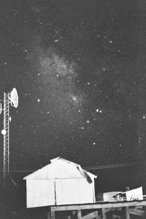 A communication tower and a small building stand under a night sky filled with stars.