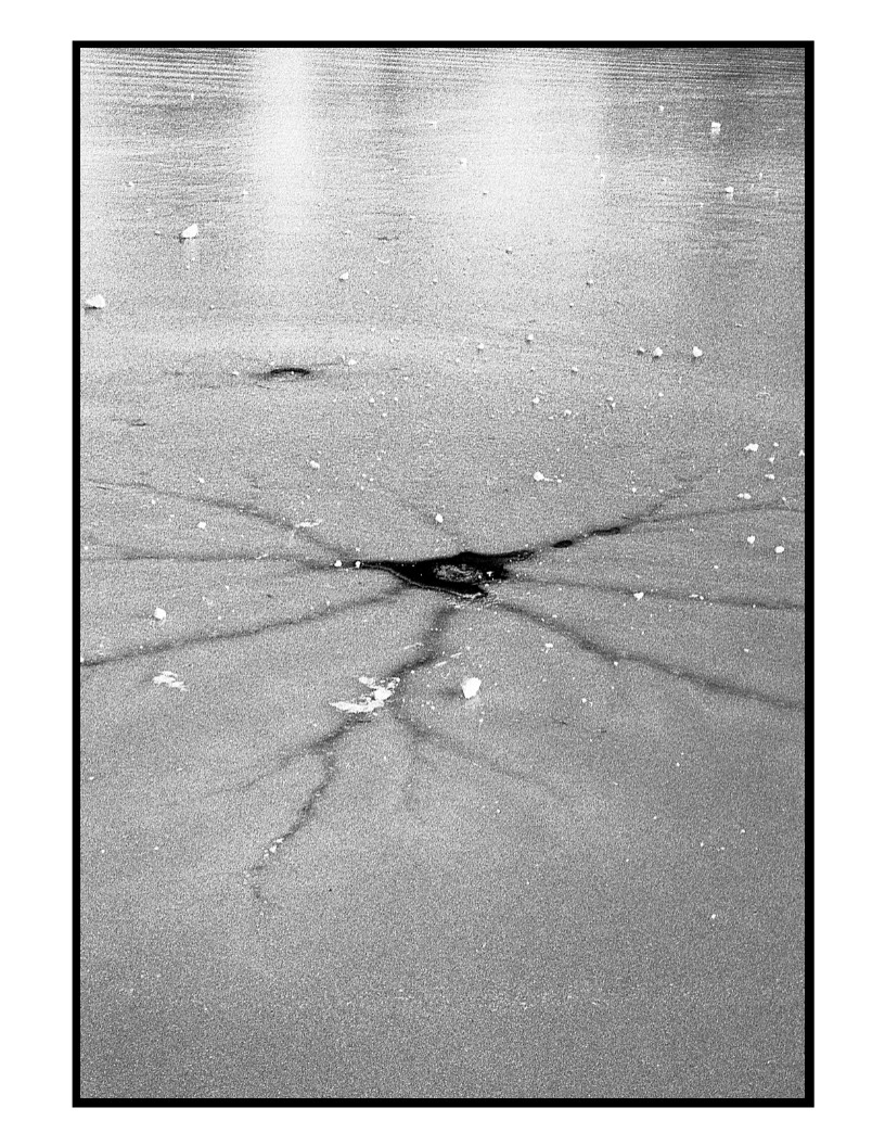 A starburst pattern of cracks radiates from a dark hole in a sheet of ice.