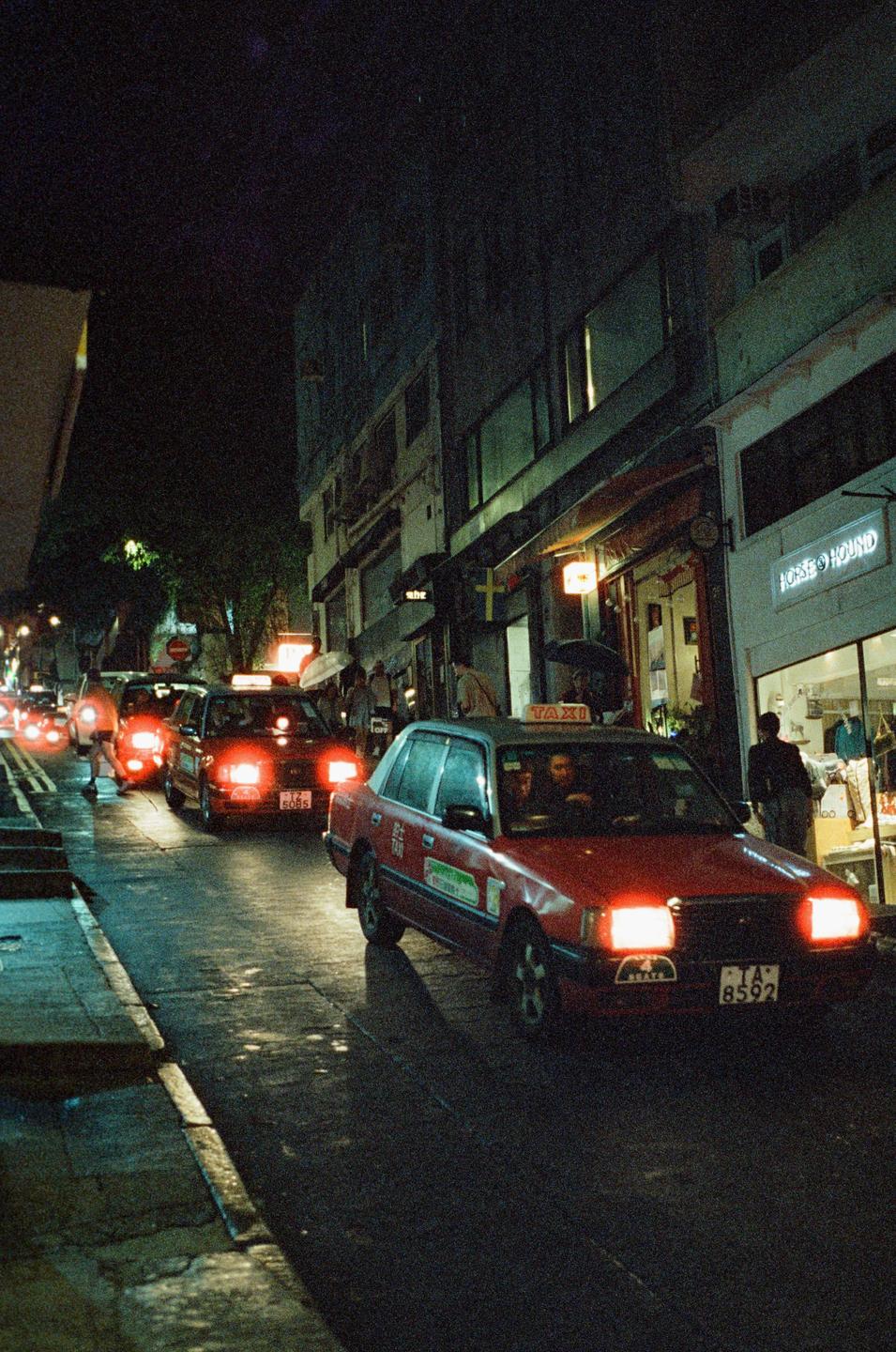 Red taxis drive down a wet street at night in Hong Kong.