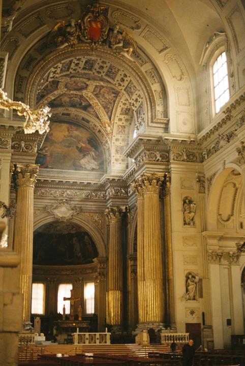 Sunlight illuminates the ornate interior of a church with tall columns and painted ceilings.