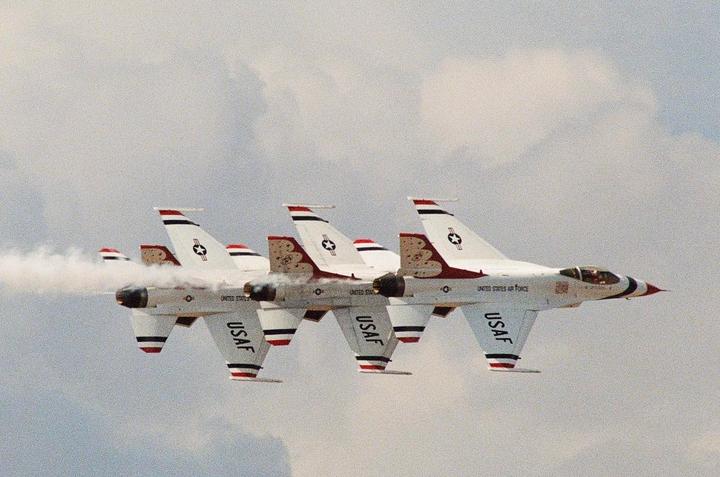 Three white and red fighter jets fly in formation, leaving a trail of smoke behind them.