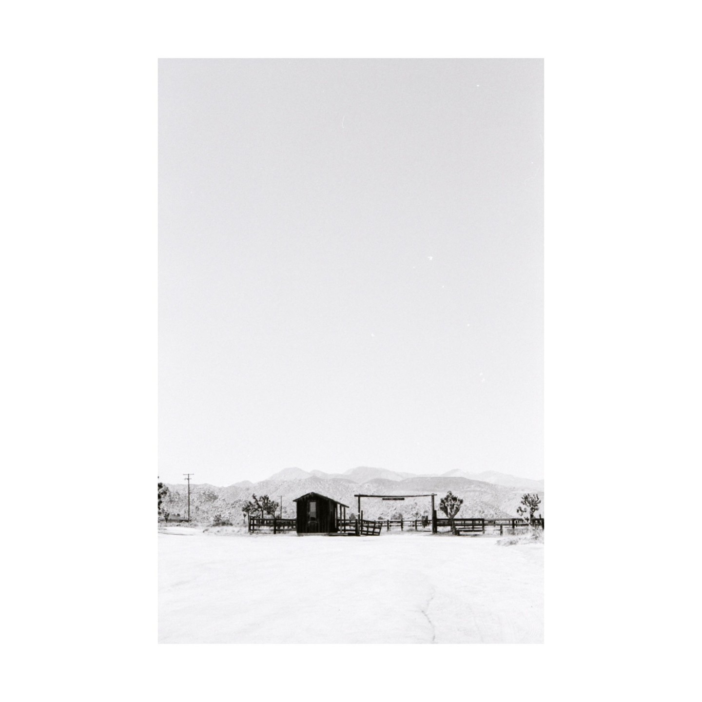 A small wooden shack and fence stand in a desert landscape with mountains in the distance.