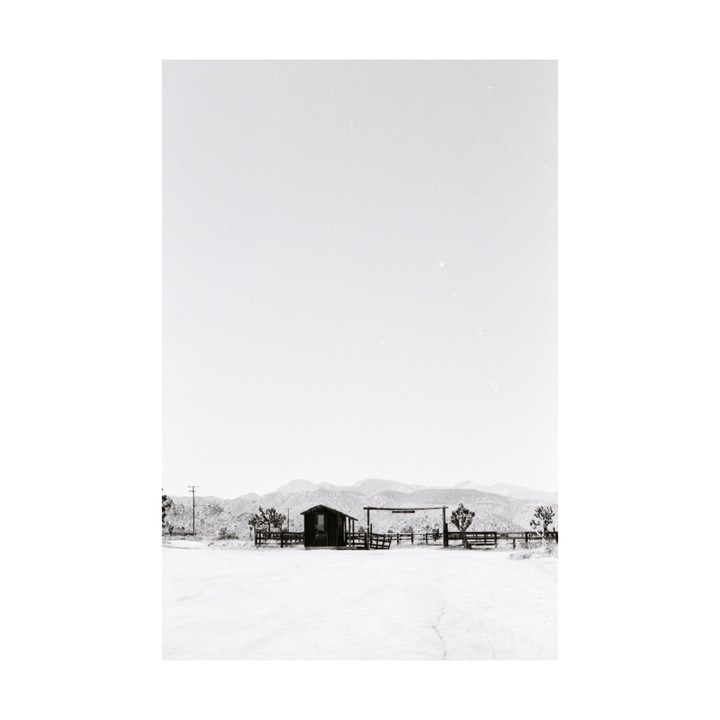 A small wooden shack and fence stand in a desert landscape with mountains in the distance.