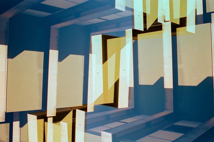 A double exposure shows a building facade with rectangular panels and shadows against a blue background.