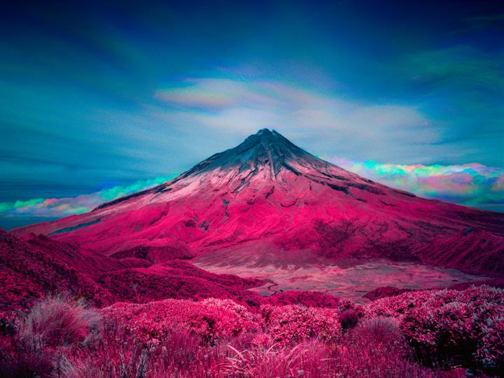 A vibrant pink mountain with a snow-capped peak stands under a blue sky with colorful clouds.