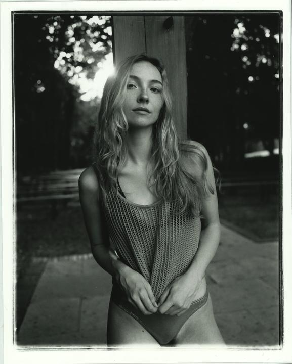 A woman with long hair and freckles stands outdoors, backlit by the sun.
