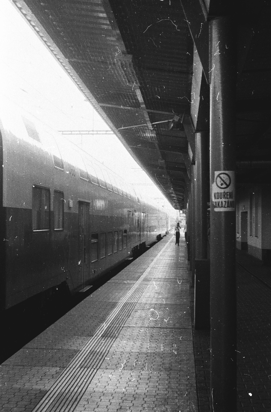 A train is stopped at a station platform with a person walking in the distance.