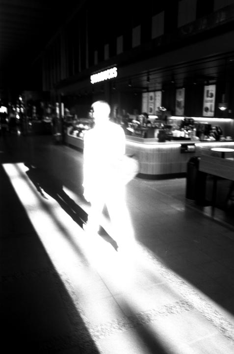 A person walks through a dark interior space with a bright light source illuminating them from the side, casting long shadows.