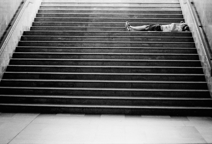 A man lies on a wide staircase with a handrail on the right.