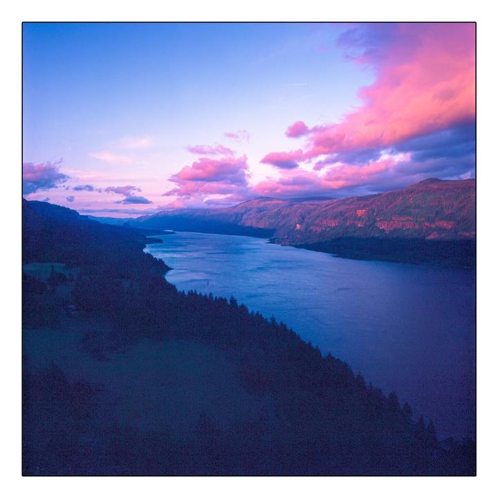 A wide river flows between two tree-covered mountains under a sky with pink clouds.