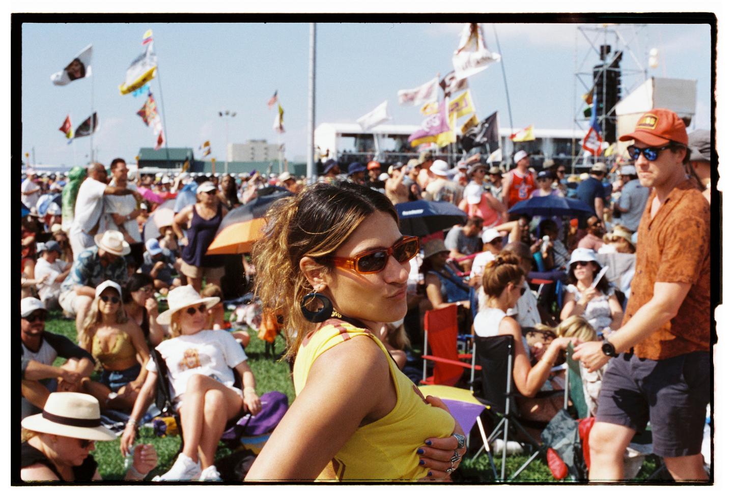 A woman in sunglasses and a yellow top poses for a candid portrait at a crowded outdoor festival.