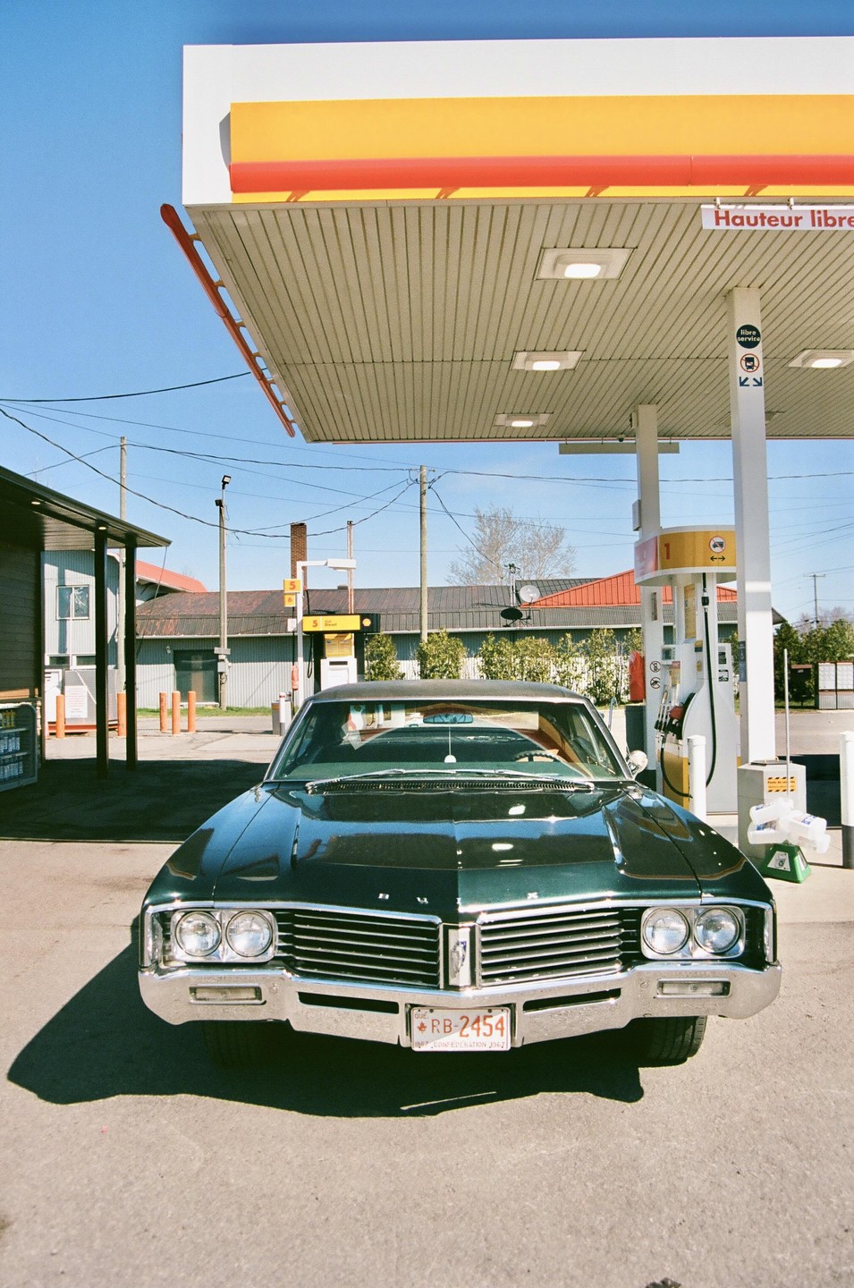 A dark green vintage car is parked at a Shell gas station.
