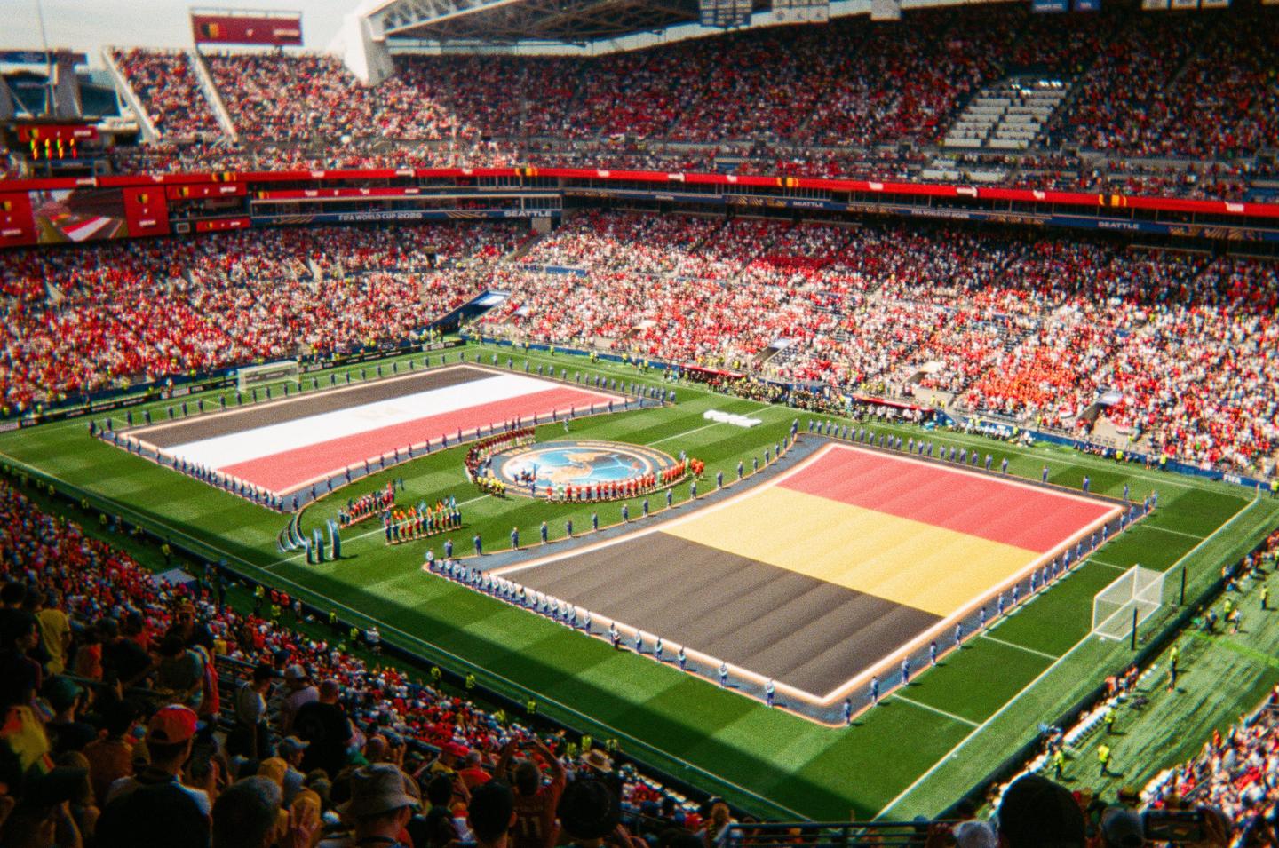 A large stadium is filled with spectators watching a soccer match between Belgium and Egypt, with large flags of both countries displayed on the field.
