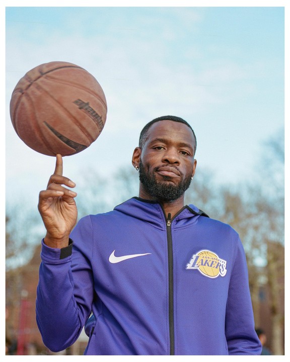 A man in a purple jacket balances a basketball on his finger.