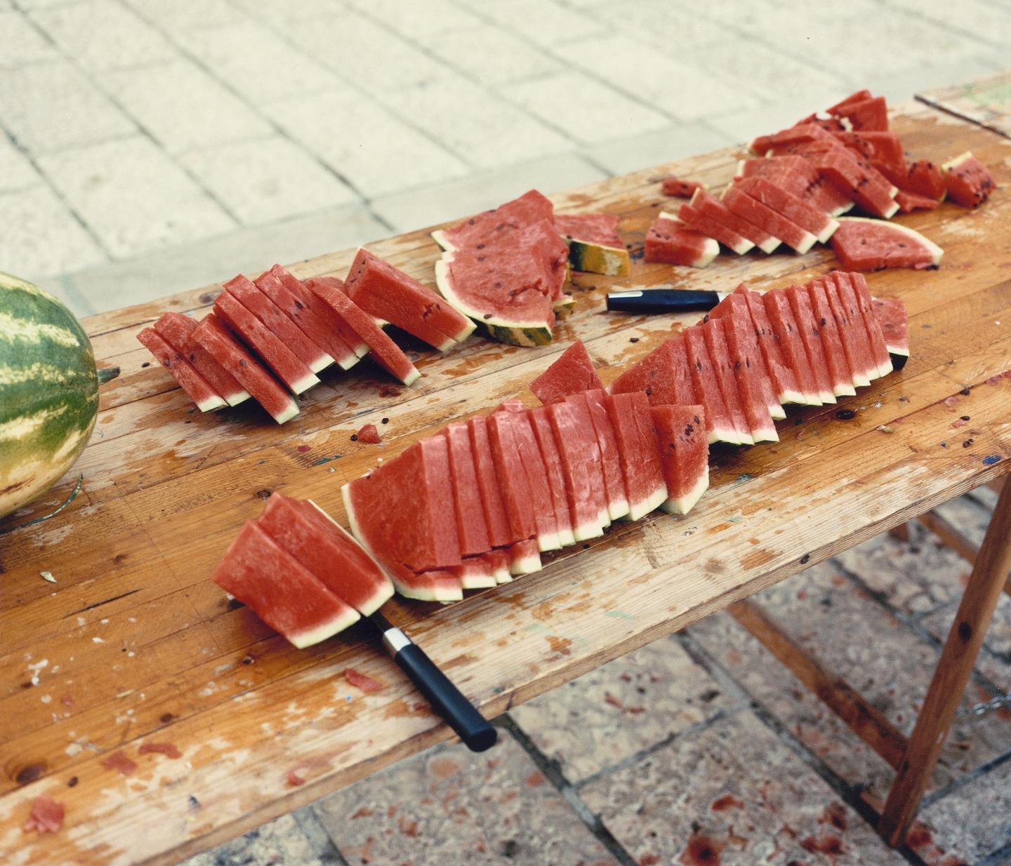 Slices of watermelon and a whole watermelon are arranged on a wooden table.
