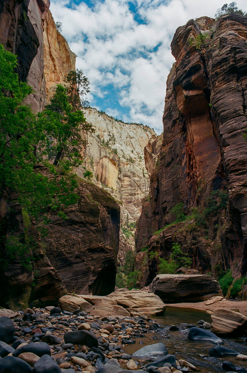 A river flows through a canyon with tall rock walls under a cloudy sky.