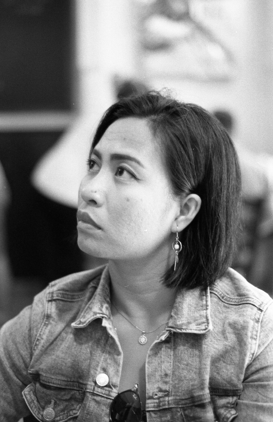 A woman with short hair and a denim jacket looks up and to the left.