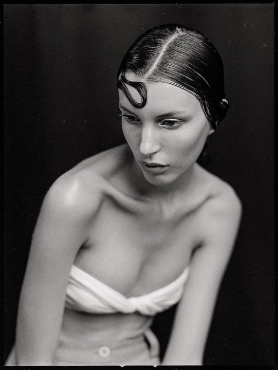 A woman with wet hair and a white top looks down and to the right.
