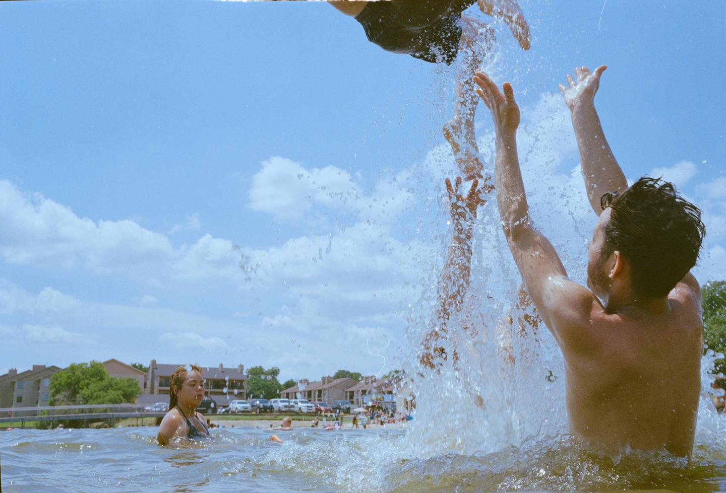 A man with his arms raised is being splashed by water while a woman floats in the water nearby.