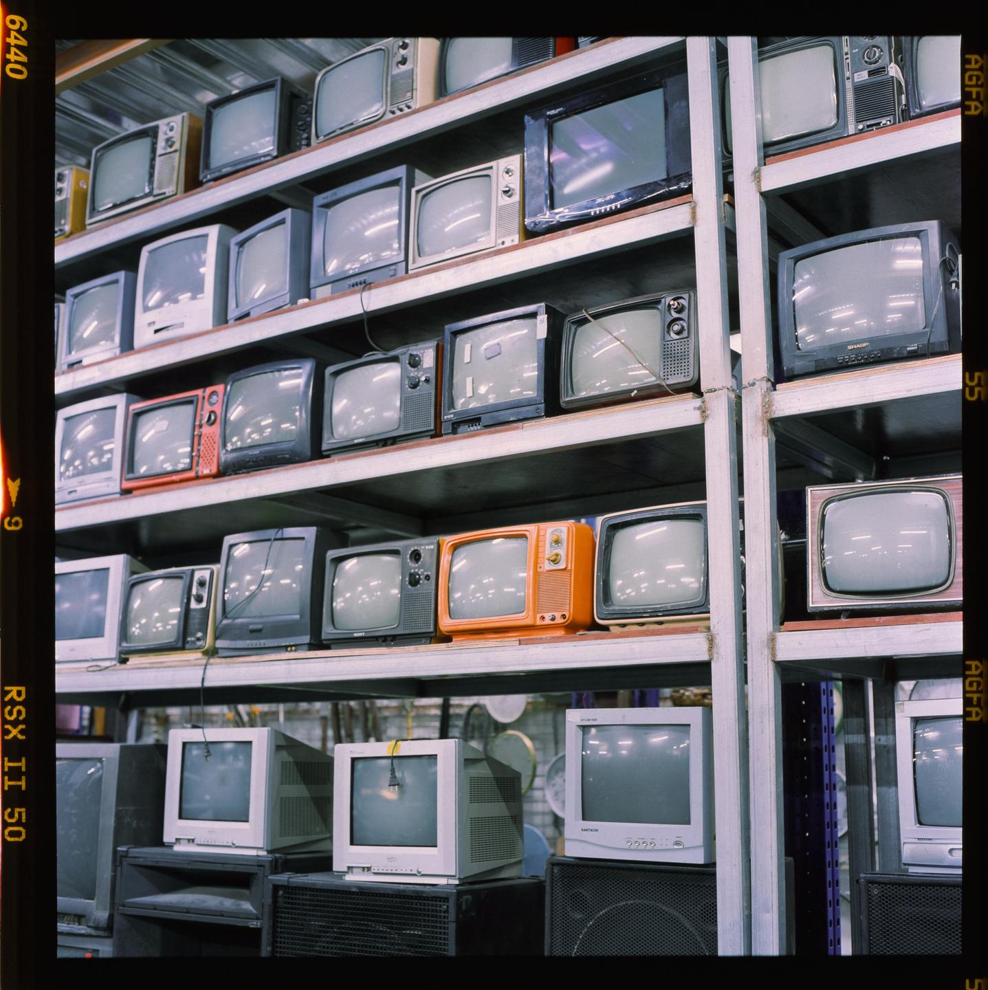 A large collection of vintage televisions are displayed on metal shelves.