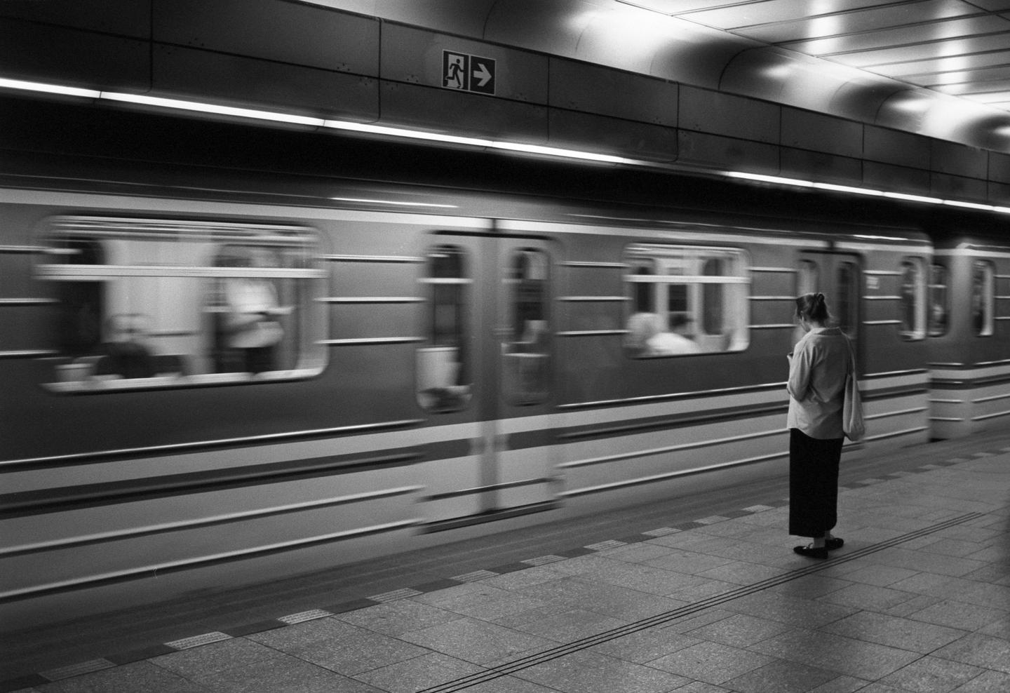 A woman stands on a subway platform as a train passes by.
