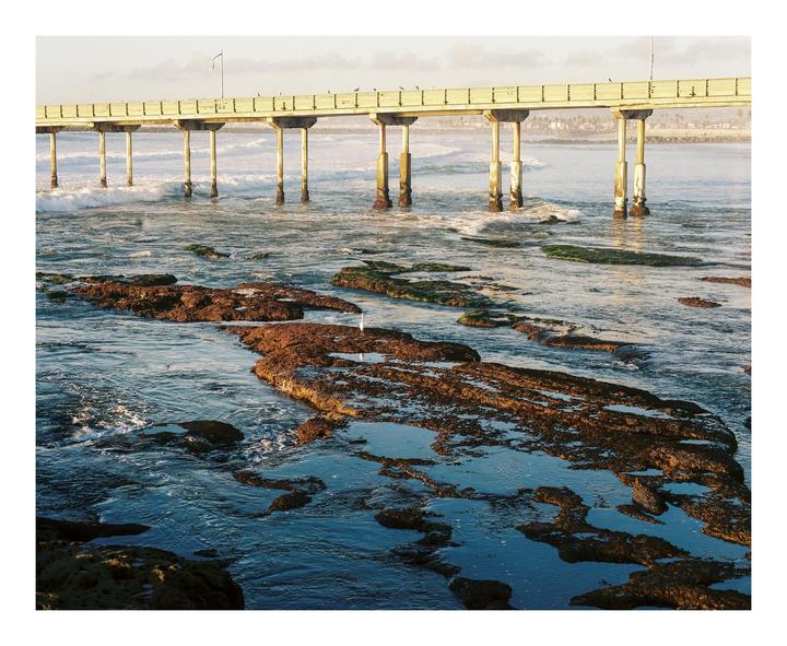 A pier extends over a rocky beach with waves crashing against the shore.