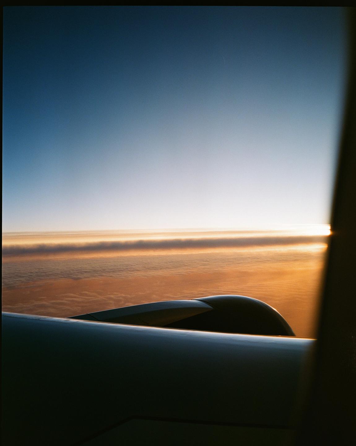 An airplane wing and engine are visible above clouds during sunset.