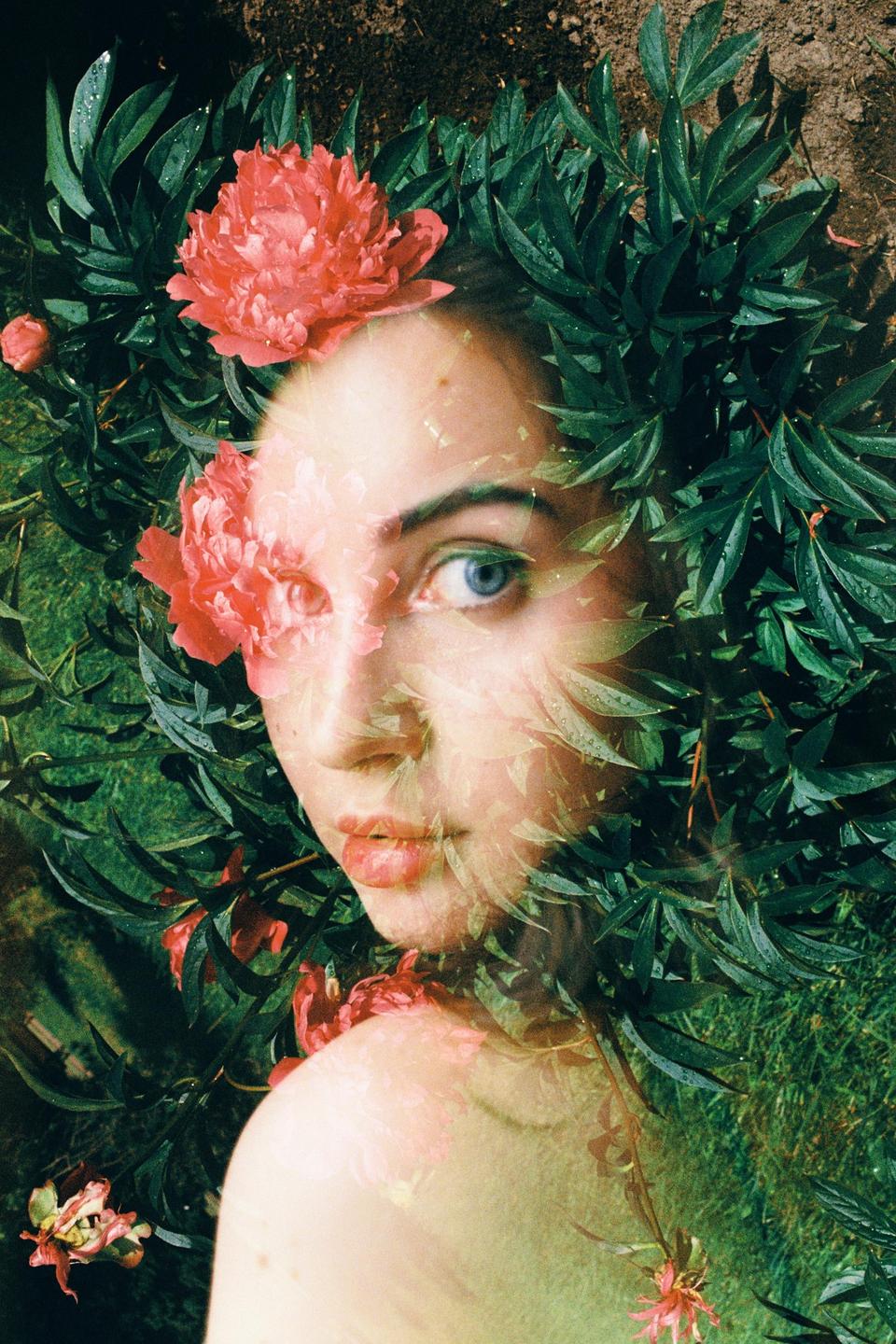 A woman's face is visible through a double exposure with green leaves and pink flowers.