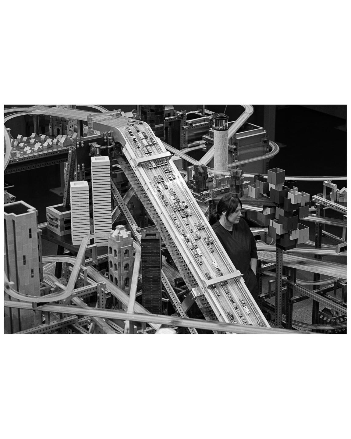 A woman stands next to a large, intricate model of a city with many roads and buildings.