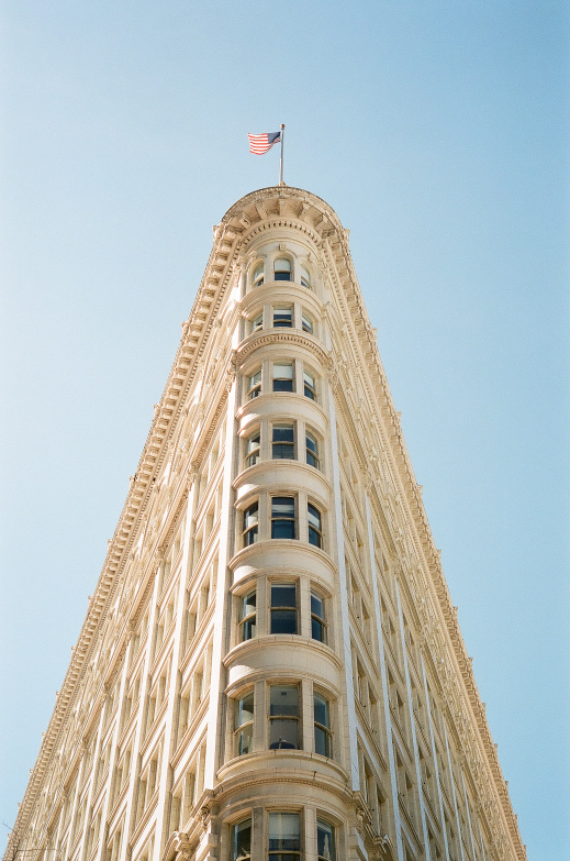 A low-angle view shows the ornate facade of the Phelan Building with an American flag flying from its rounded corner against a clear sky.