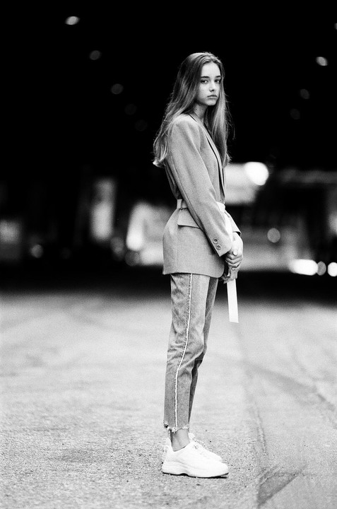 A young woman stands in the middle of a street at night, looking over her shoulder.