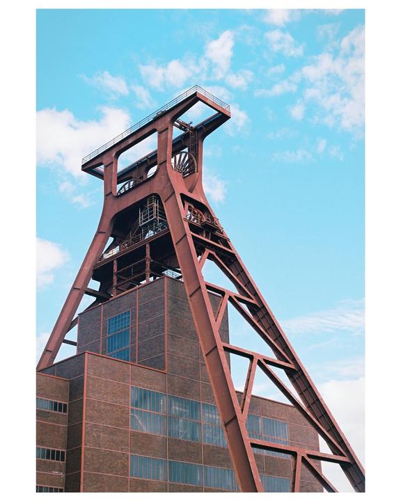 A large red industrial structure stands against a blue sky with white clouds.