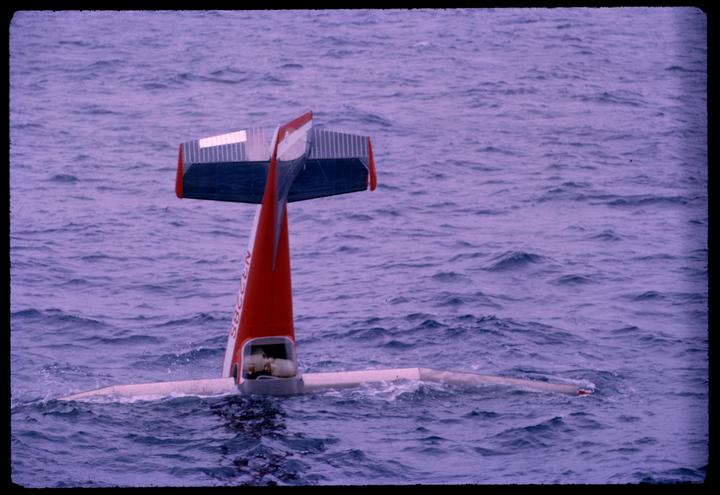 The tail of a red and white airplane sticks out of the ocean.